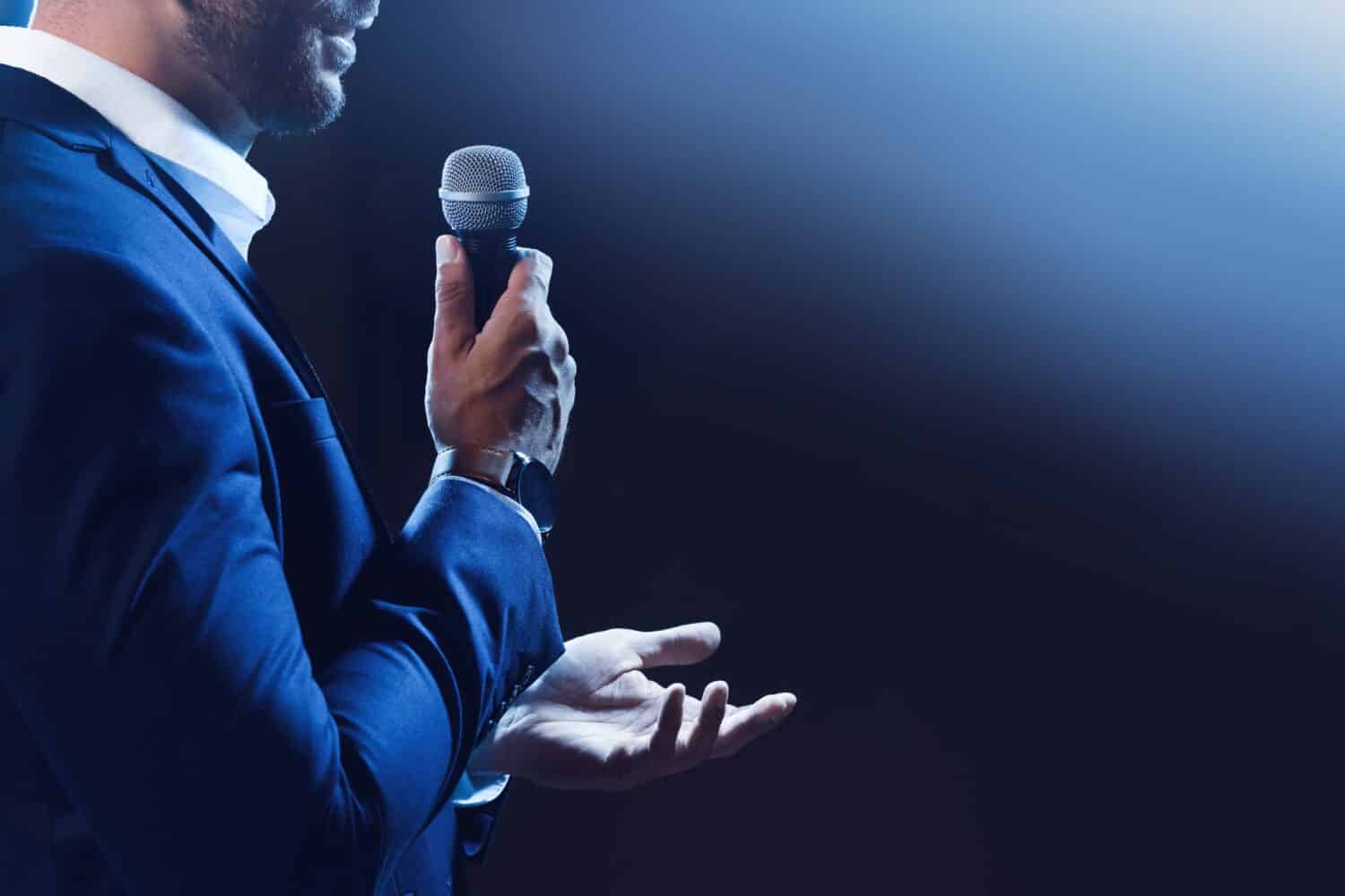 Altoparlante motivazionale con microfono che si esibisce sul palco, primo piano.  Spazio per il testo