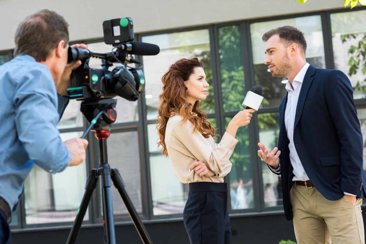 cameraman professionista e giornalista che intervistano un uomo d'affari vicino all'edificio per uffici