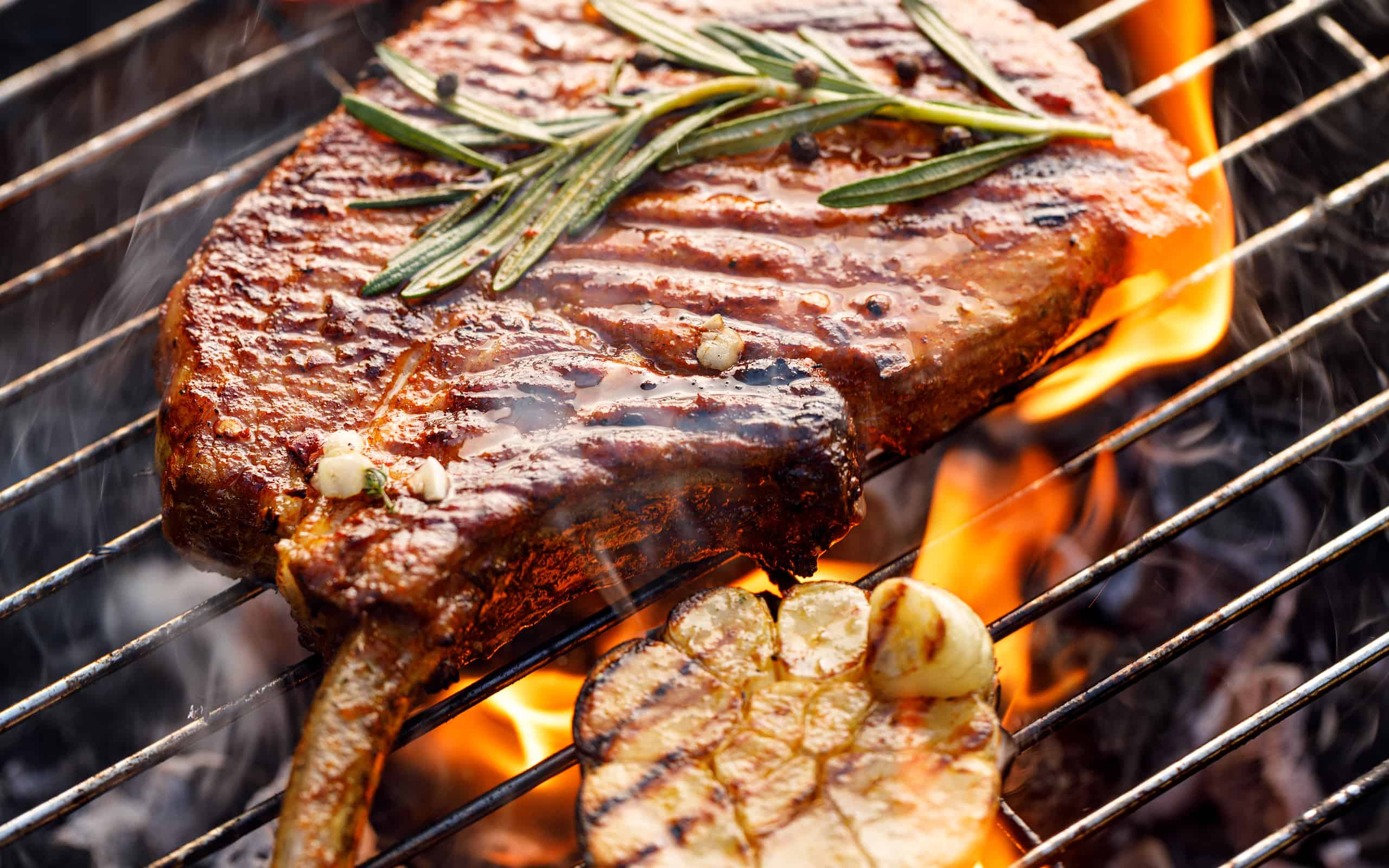 Braciola di maiale con osso alla griglia, bistecca di maiale, tomahawk in marinata piccante su una griglia fiammeggiante, primo piano.