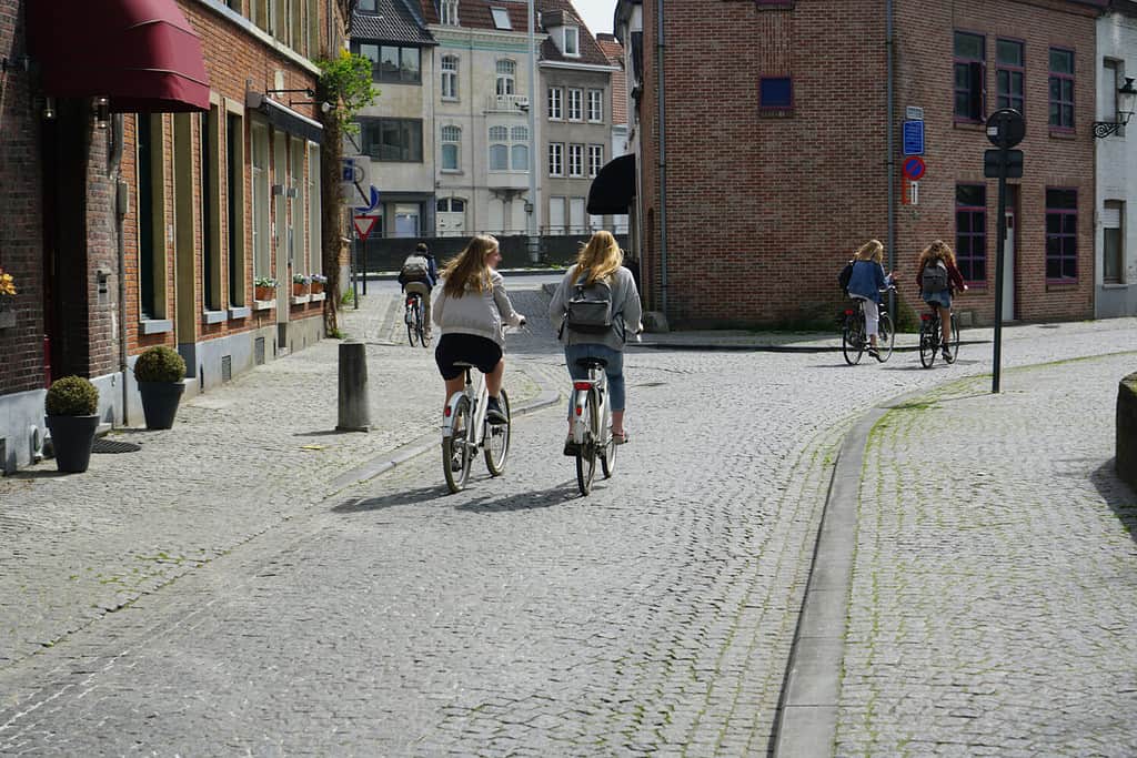 due donne in bicicletta sulla strada europea.  dietro di due ciclisti.  2 amiche cavalcano su un ciottolo in bicicletta sullo sfondo dell'edificio dell'hotel.  Noleggio bici in città.  Anversa, Belgio.