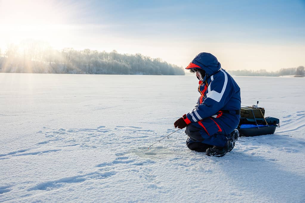 Un pescatore sta pescando con una canna da spinning invernale su un lago ghiacciato.  Concerto di pesca sul ghiaccio.