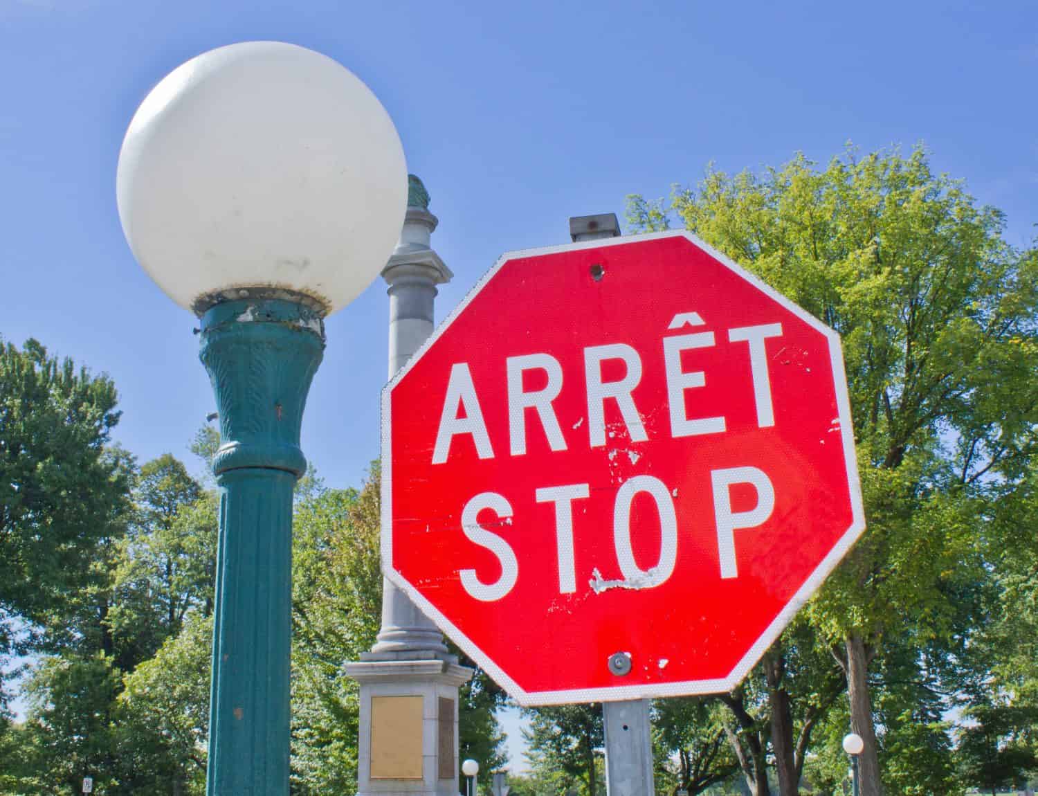 Un segnale di stop bilingue francese e inglese, rosso e bianco accanto a un classico lampione all'ingresso di un parco a Quebec City, Canada.