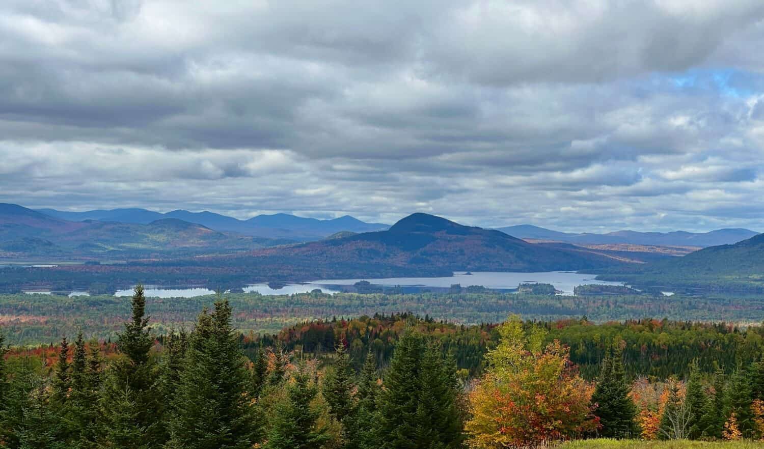 Una veduta aerea di alberi autunnali vicino a un lago e montagne a Jackman, nel Maine