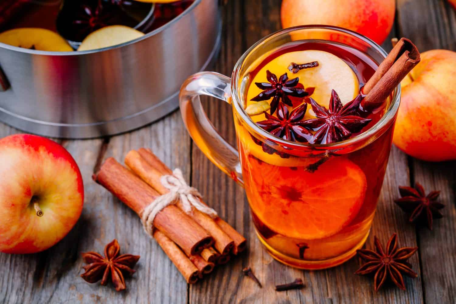 Sidro di mele caldo con bastoncini di cannella, chiodi di garofano e anice su fondo di legno