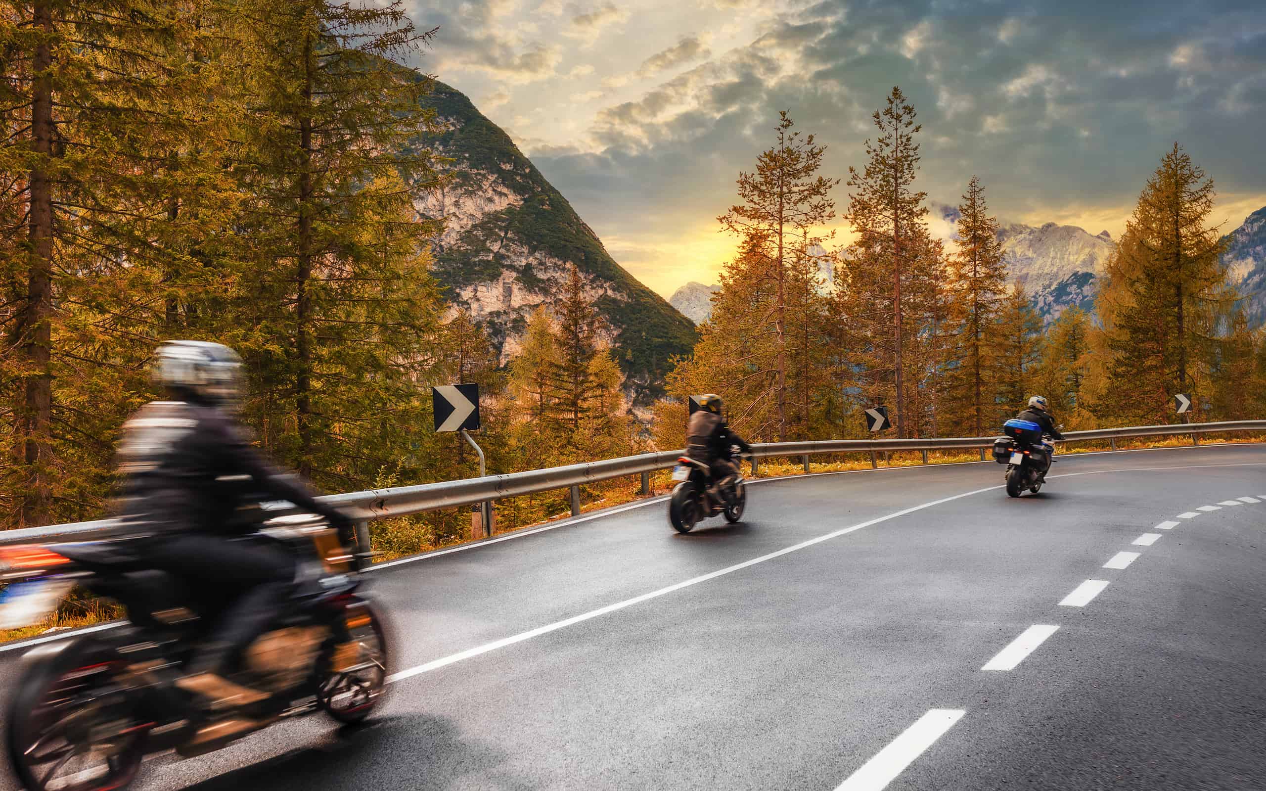 Concetto di viaggio.  Gruppo di persone che viaggiano in motocicletta su una strada asfaltata in montagna al tramonto nelle Alpi italiane Bellissimo paesaggio autunnale