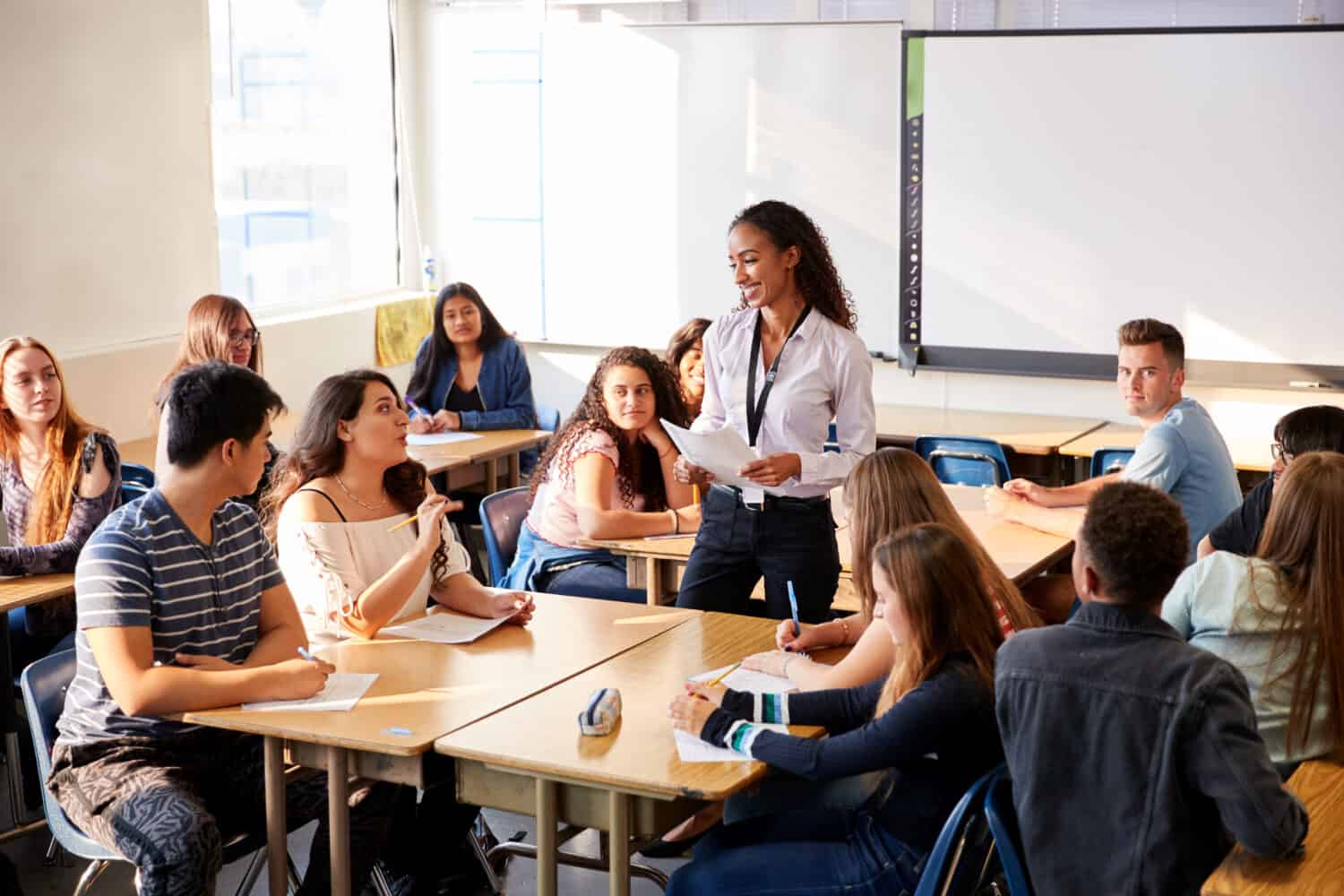 Insegnante di scuola superiore femminile in piedi accanto alla lezione di insegnamento del tavolo degli studenti