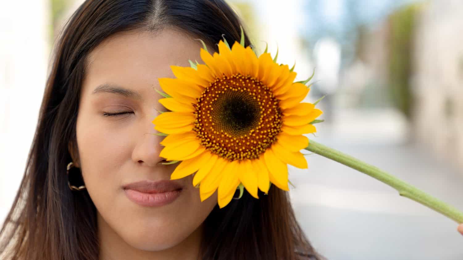 Giovane donna, sorridente e con in mano un girasole in una soleggiata giornata primaverile in un parco, messa a fuoco selettiva, concetto di gioia e fioritura in primavera.  Pace, girasoli giganti e gialli.