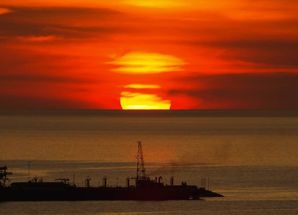 Grande tramonto rotondo nascosto dietro le nuvole sopra l'orizzonte sul Golfo del Messico (dal Messico Campache) con la sagoma di una grande nave