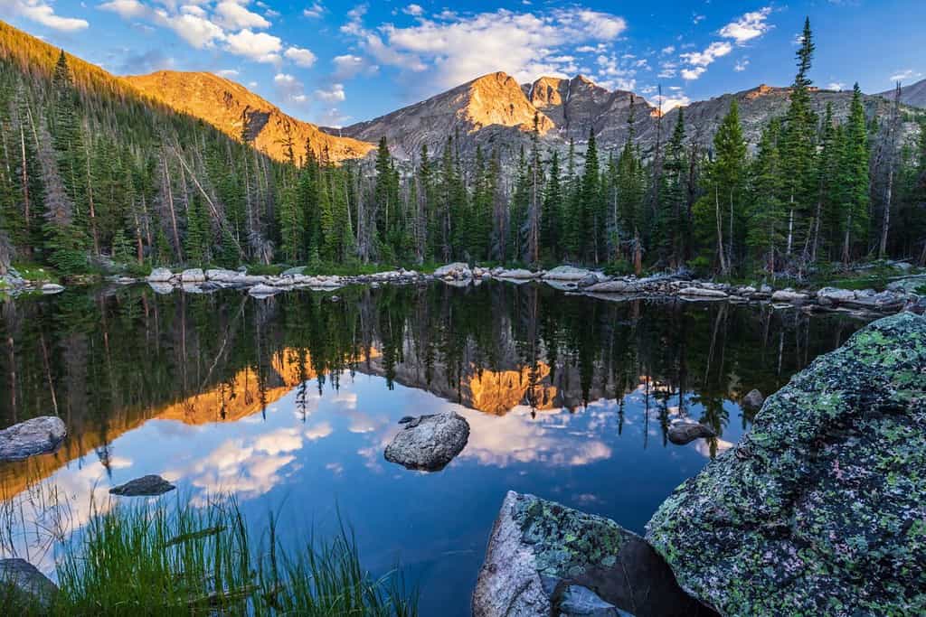 I massi circondano le acque calme del lago Chipmunk che riflettono il monte Ypsilon e il monte Chiquita illuminati dalla luce del mattino nel Parco Nazionale delle Montagne Rocciose, in Colorado.