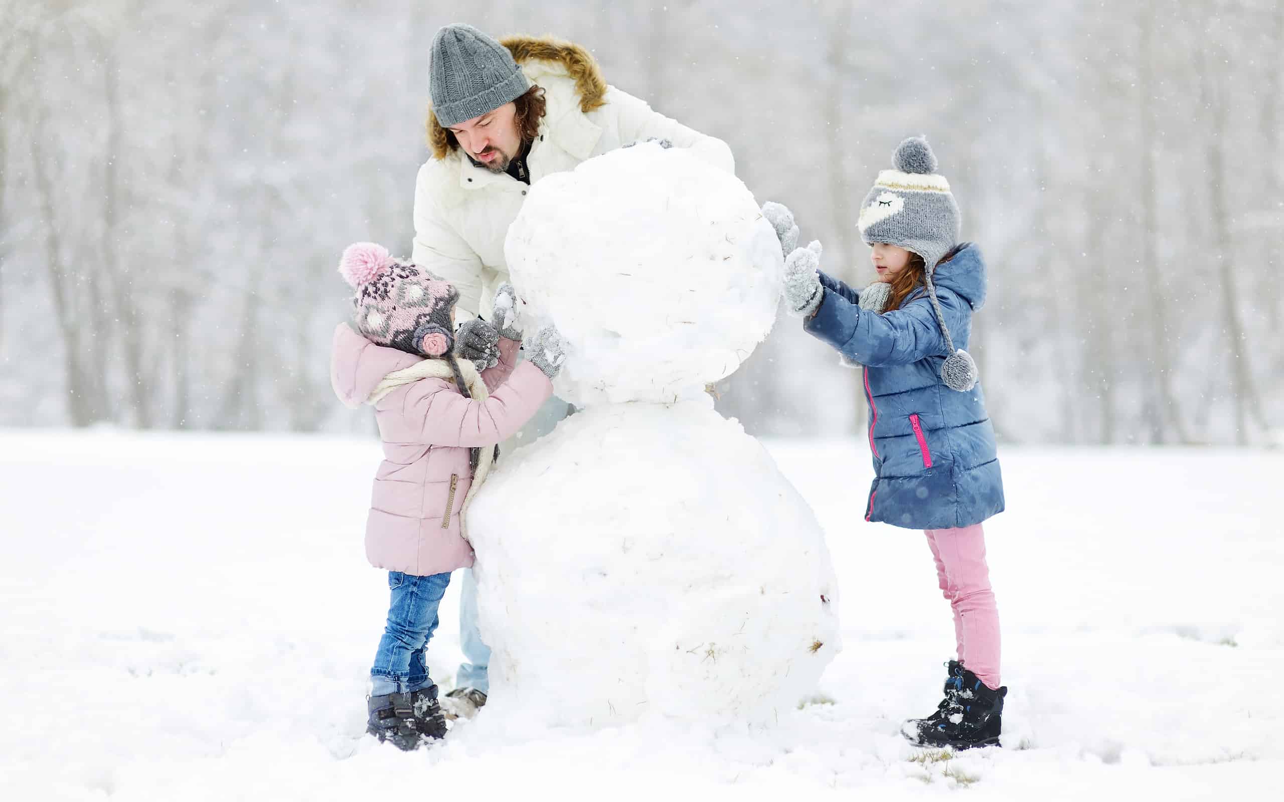 Giovane padre e le sue figlie che costruiscono un pupazzo di neve