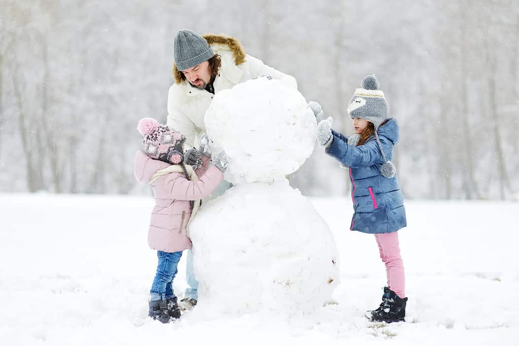 Giovane padre e le sue figlie che costruiscono un pupazzo di neve