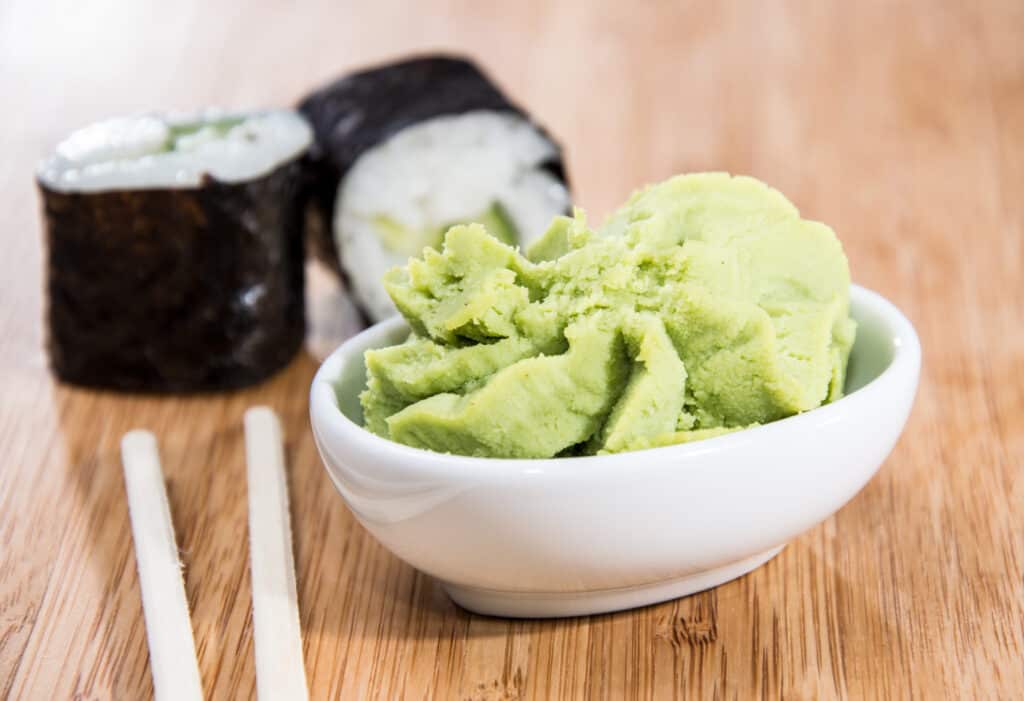 Ciotola bianca di wasabi verde chiaro con due California Rolls e un paio di bacchette