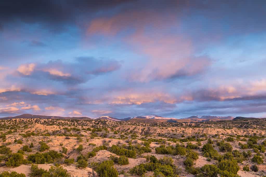 Nuvole colorate drammatiche su un paesaggio desertico e montano al tramonto