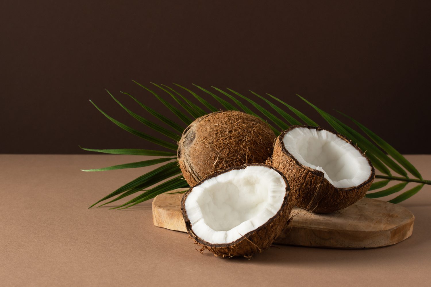 Noci di cocco con foglia di palma su sfondo marrone.  Frutta tropicale.