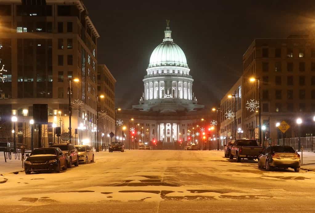 Madison, la capitale del Wisconsin, vista sulla strada del centro con auto parcheggiate e il Campidoglio dello stato del Wisconsin che brilla nella notte di bufera di neve.  Stato del Wisconsin, Midwest degli Stati Uniti.  Bella notte invernale nevosa.