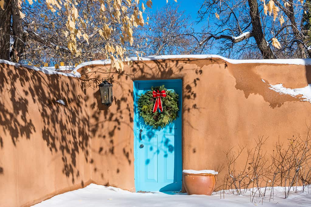 Ghirlanda di Natale sulla porta turchese nel muro di mattoni innevati, Santa Fe, New Mexico