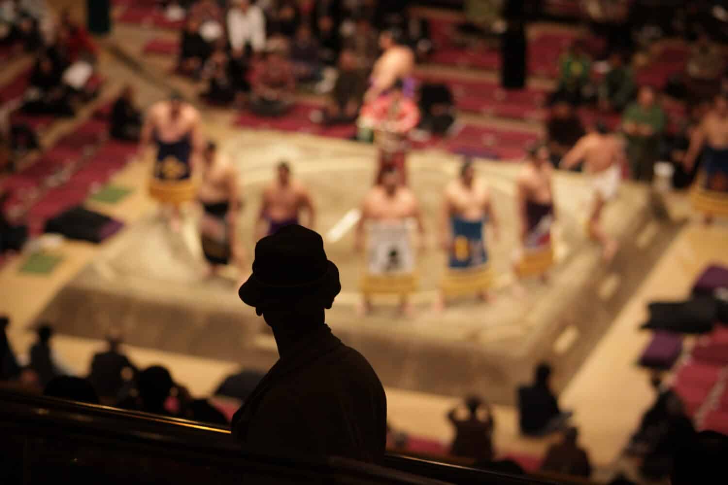 Silhouette di un uomo anziano che guarda i lottatori di sumo in piedi in un anello cerimoniale