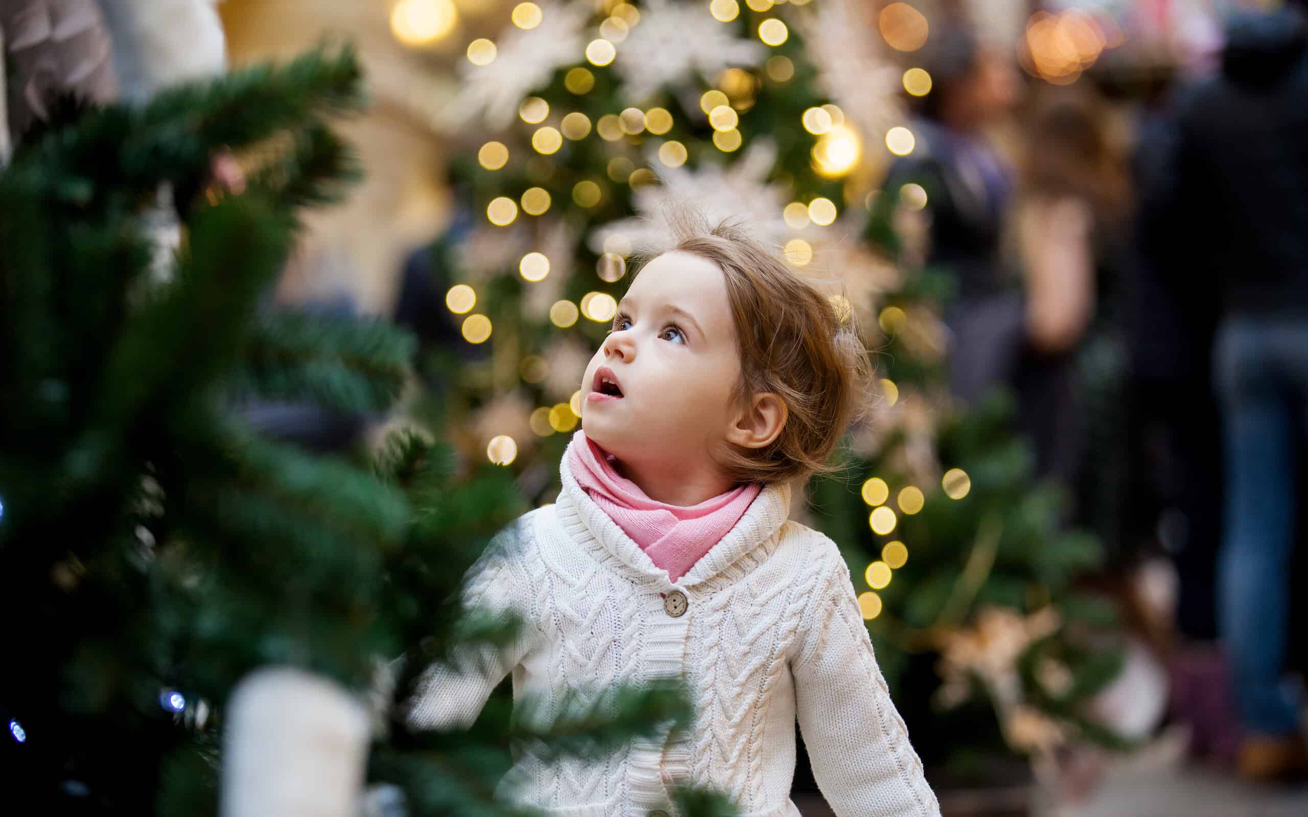Bambina sveglia che esamina gli alberi di Natale