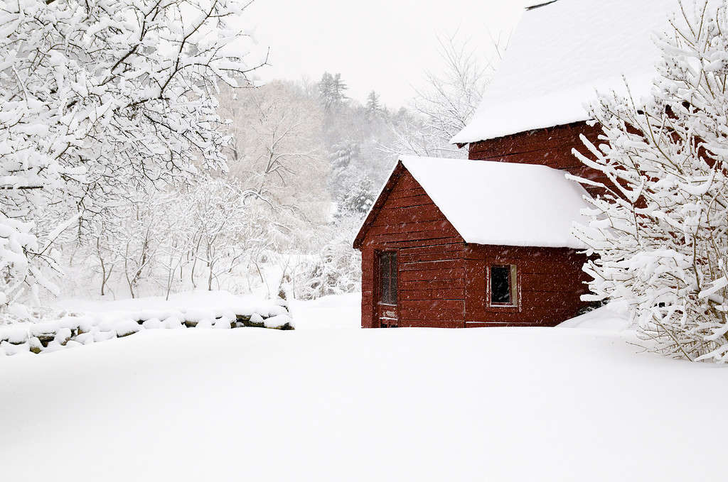 Fienile nella neve con muro di pietra e alberi