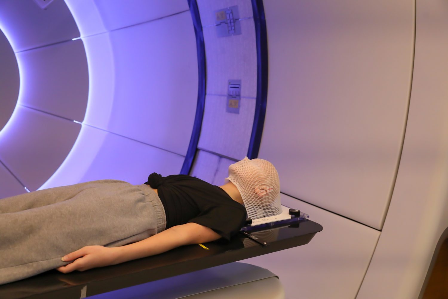 Radioterapia protonica.  Paziente bambino con cancro al cervello sdraiato sul letto di posizionamento con maschera di fissaggio sulla testa nella sala di trattamento.