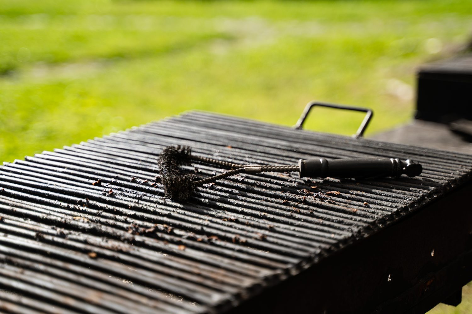 vista frontale primo piano della griglia per barbecue vuota all'aperto con spazzola nera per pulire la parte superiore in ambiente esterno con erba verde