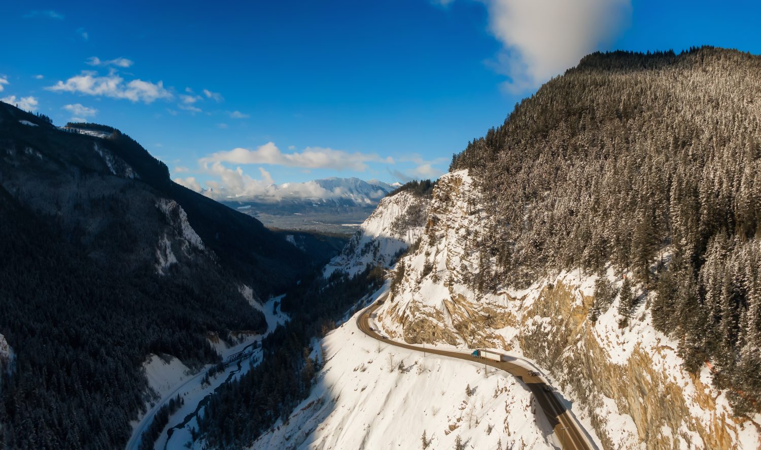 Vista panoramica aerea di un'autostrada panoramica nella valle tra il paesaggio montano canadese durante l'alba soleggiata invernale.  Preso vicino a Golden, British Columbia, Canada.