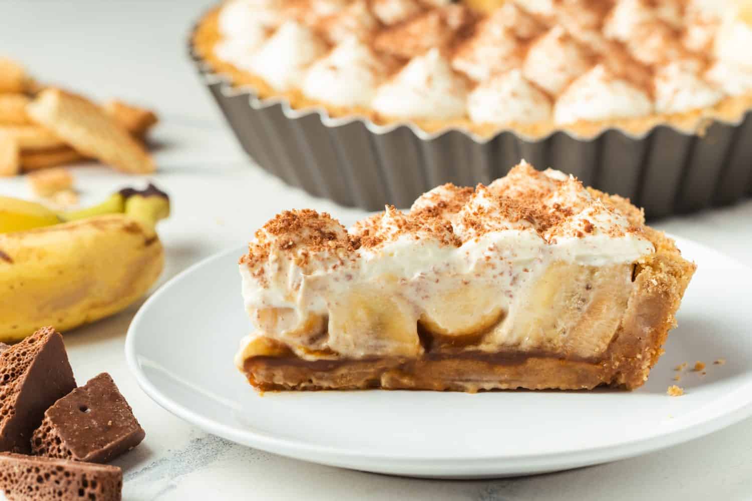 Torta al caffè con ripieno di salsa di banane e caramello cosparsa di cioccolato fondente grattugiato su sfondo di marmo bianco.  Torta tradizionale inglese