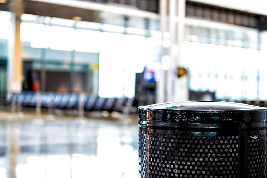 Interno dell'aeroporto con bidone della spazzatura nero in primo piano e sfondo bokeh sfocato dell'area di attesa al cancello di partenza senza nessuno vuoto