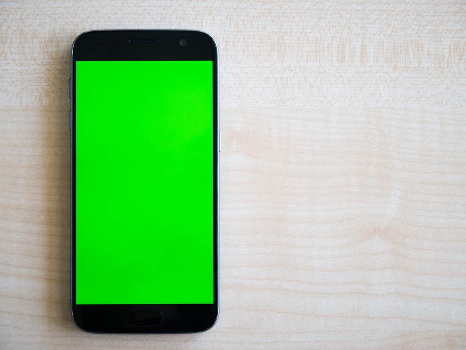 Smartphone Android con schermo verde orientato verticalmente, girato dall'alto verso il basso sul tavolo di legno