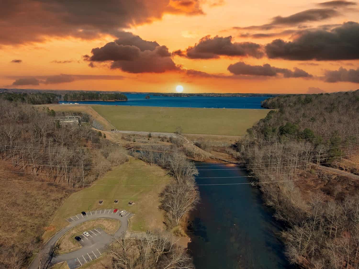 Una ripresa aerea delle acque correnti del fiume presso la Lower Pool West sul Lago Lanier con alberi spogli d'inverno e potenti nuvole al tramonto a Cummings Georgia USA