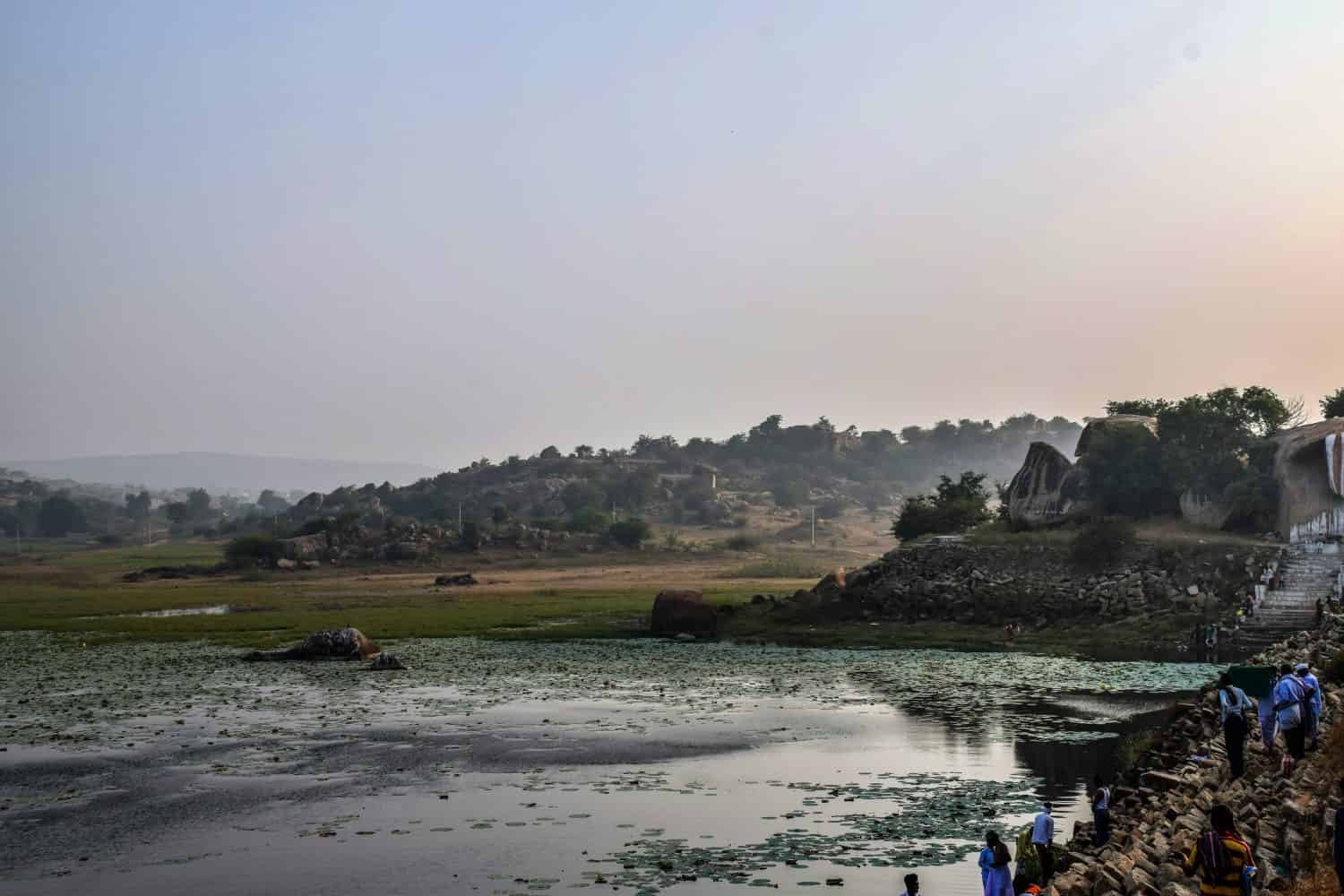   Foto d'archivio della riva del fiume sacro Bhima vicino al tempio di Lord Mallaya, persone che fanno il bagno rituale la mattina presto.  fiume circondato da rocce e alberi verdi, a Mailapur, Yadgir, Karnataka, India.