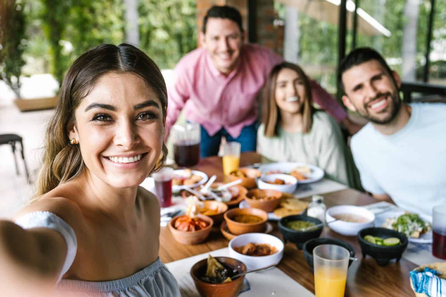 Donna messicana che scatta un selfie fotografico con un gruppo di amici latini e mangia cibo messicano nella terrazza del ristorante in Messico America Latina