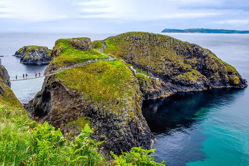 Vista dal ponte di corda di Carrick-a-Rede, famoso ponte di corda vicino a Ballintoy nella contea di Antrim, Irlanda del Nord, sulla costa irlandese.  Attrazione turistica, ponte verso la piccola isola in una giornata nuvolosa.