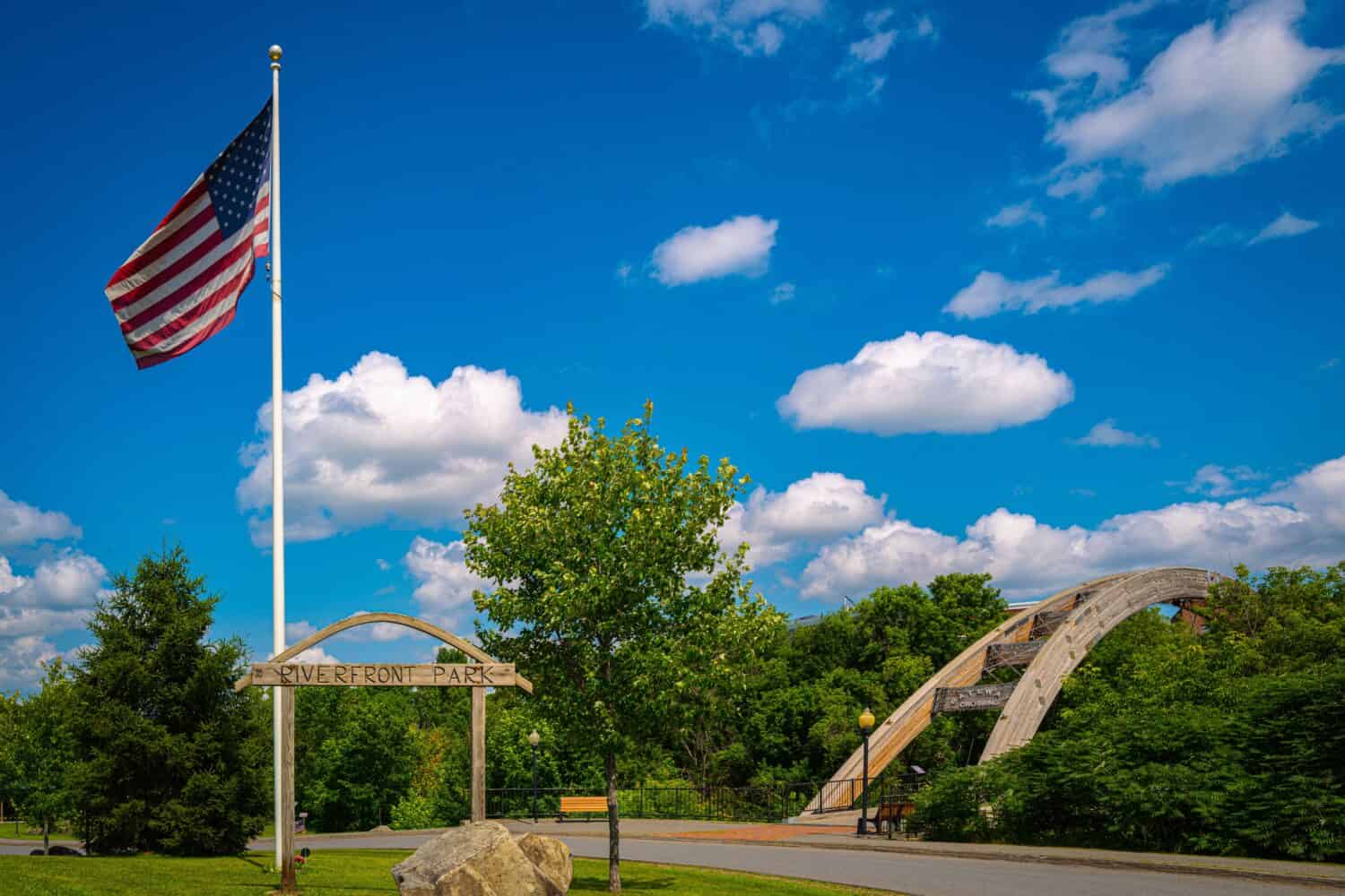 Houlton Riverfront Park nella contea di Aroostook, nel Maine settentrionale, in una giornata estiva con la bandiera americana che sventola nel vento e la vista del ponte ad arco Gateway Crossing