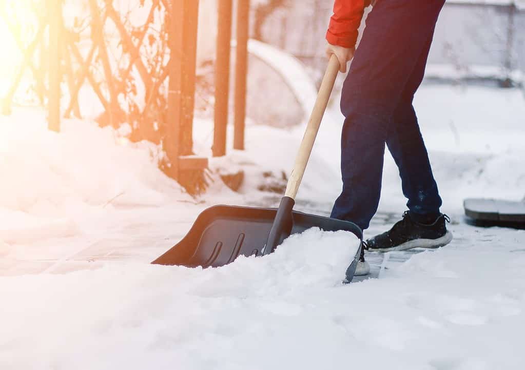 un impiegato del servizio pubblico in una sola pala di neve nella bufera di neve invernale.  appoggiato sulla neve con una pala nel vialetto.  cumuli di neve.