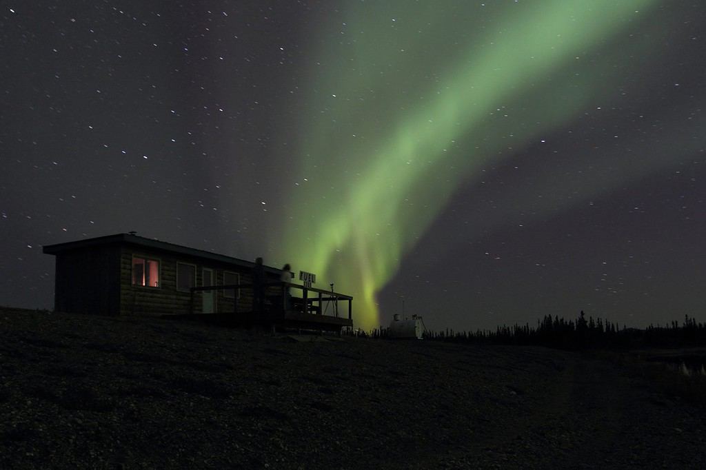 L'aurora boreale brilla di verde e giallo su una capanna sul lago a Bettles Field in Alaska