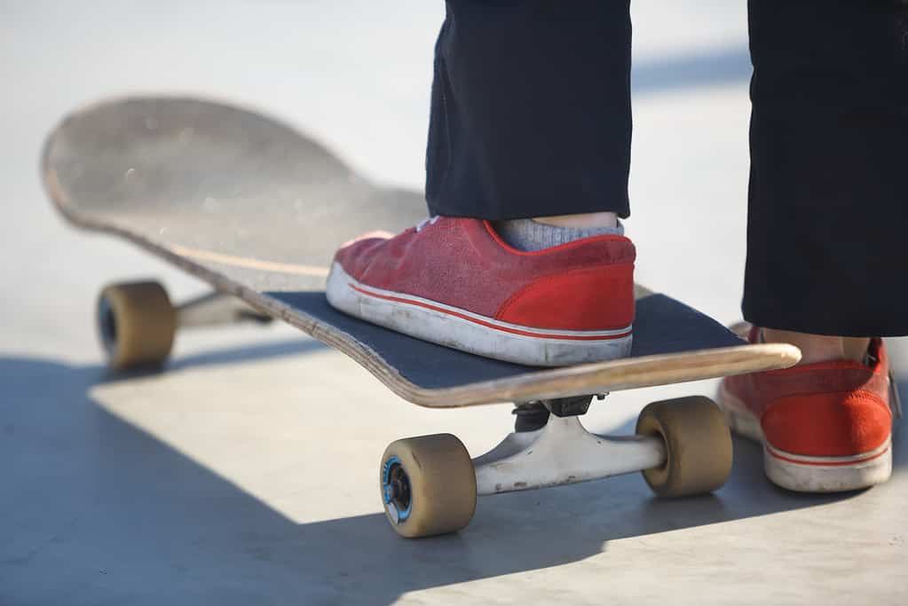 Ragazza teenager del pattinatore che sta sul vecchio ponte dello skate board nello skatepark pronto a pattinare.  Piedi di giovane atleta skateboarder femminile che pattina nel parco all'aperto