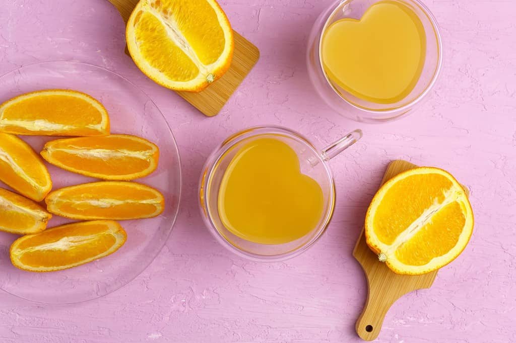 Bicchiere di succo d'arancia con vista dall'alto delle arance, sfondo rosa amaranto.  Disposizione piatta.  Amore per la frutta, cibo sano