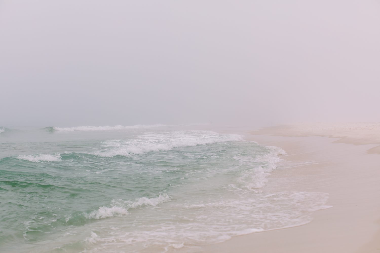 Onde color verde acqua che si infrangono sulla nebbiosa spiaggia nebbiosa di Pensacola in Florida.	