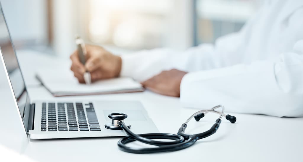 Laptop, stetoscopio e medico scrivono su un taccuino per la pianificazione della ricerca o l'innovazione della tecnologia medica nell'ufficio ospedaliero.  Operatore medico sanitario, appunti sul libro della strategia di ricerca e comunicazione online