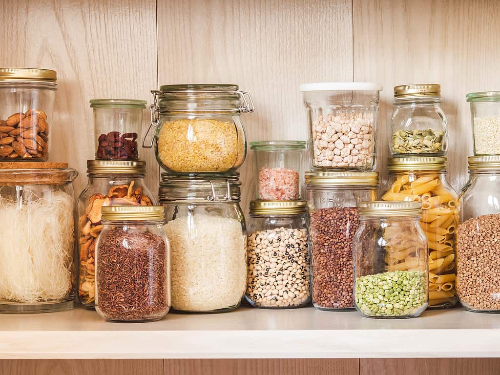 Mensola in cucina con vari cereali e semi: piselli spezzati, semi di girasole e di zucca, fagioli, riso, pasta, farina d'avena, cuscus, lenticchie, bulgur in barattoli di vetro