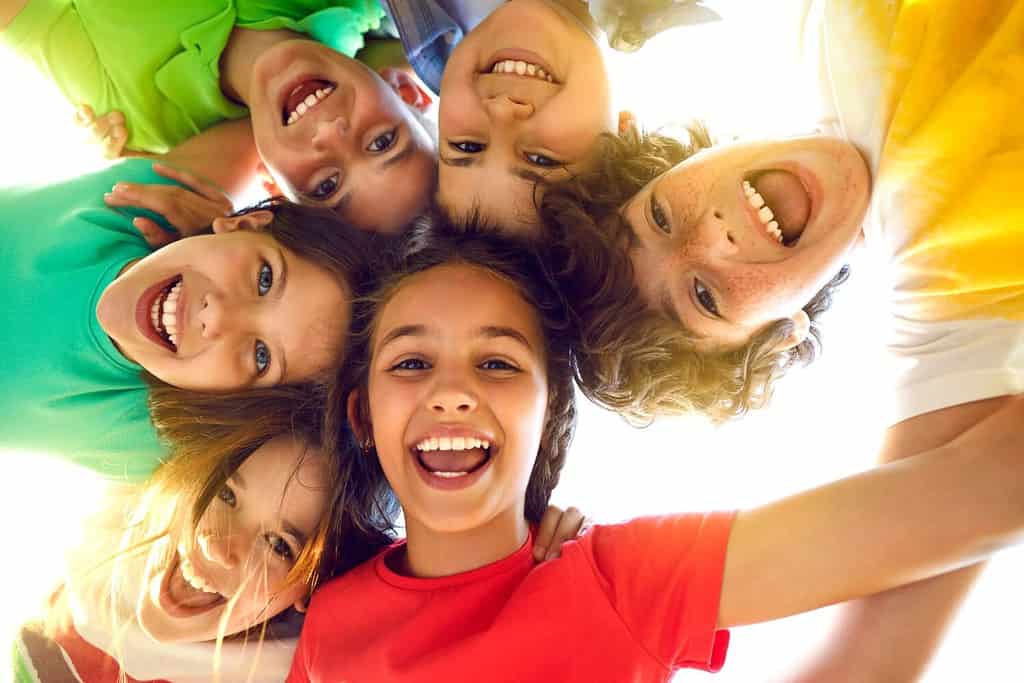 Gruppo di bambini allegri, gioiosi e carini che giocano insieme e si divertono.  Ritratto di gruppo di bambini felici che si stringono, guardando la telecamera e sorridendo.  Angolo basso, vista dal basso.  Concetto di amicizia