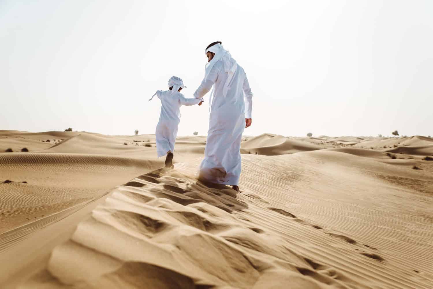 Padre e figlio mediorientali che indossano il tradizionale kandura arabo trascorrono del tempo nel deserto, Dubai