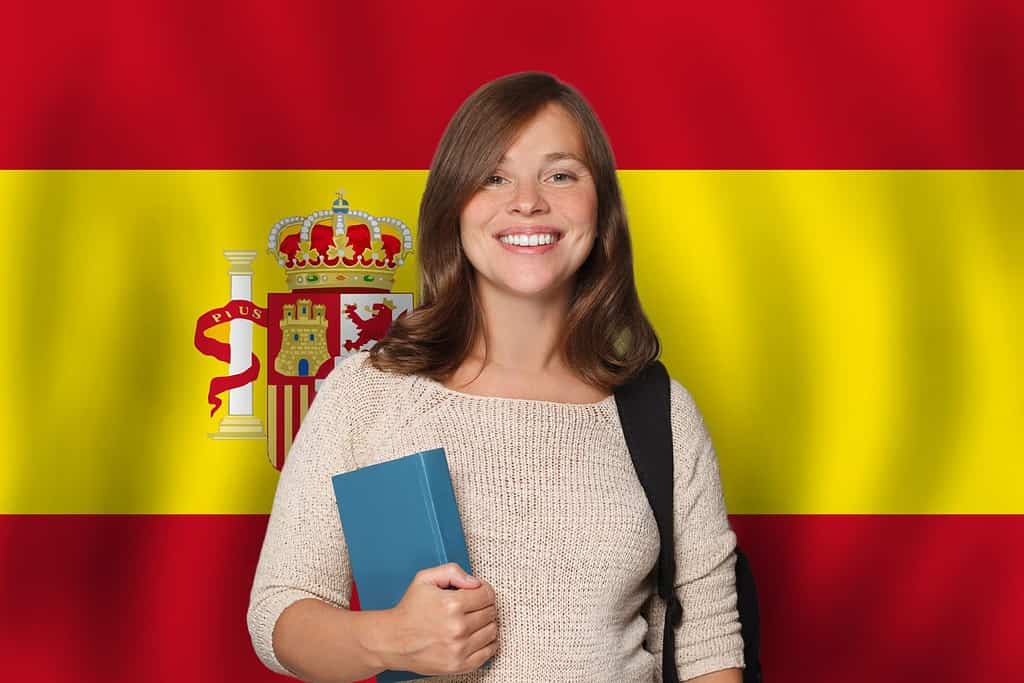 Studentessa allegra sullo sfondo della bandiera spagnola.  Viaggiare, studiare e imparare la lingua nel concetto di Spagna