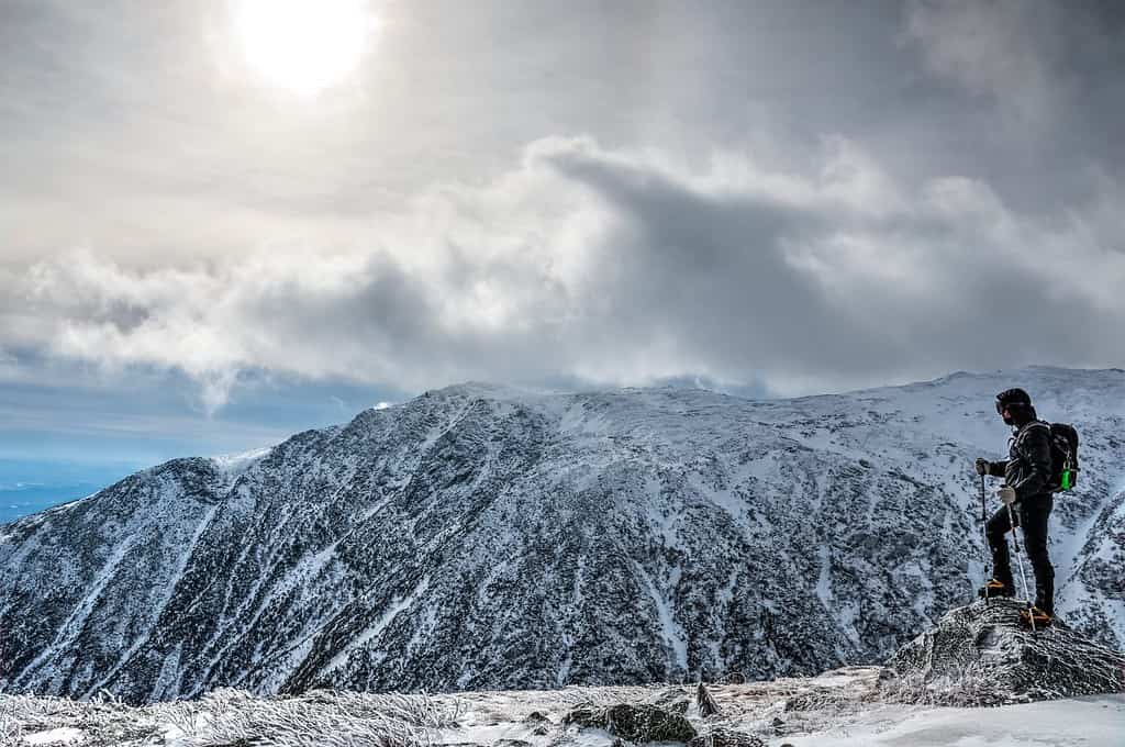 Uomo con l'attrezzatura al limite, che fa un'escursione sul monte Washington in inverno, guardando oltre il burrone.  New Hampshire, Stati Uniti