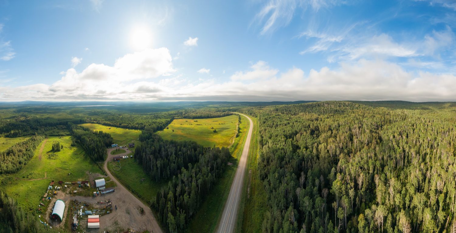 Vista panoramica sulla strada vicino al tramonto, circondata da foreste, terreni agricoli e industria.  Ripresa aerea del drone.  A nord-ovest di Fort Nelson, Alaska Highway, Columbia Britannica settentrionale.