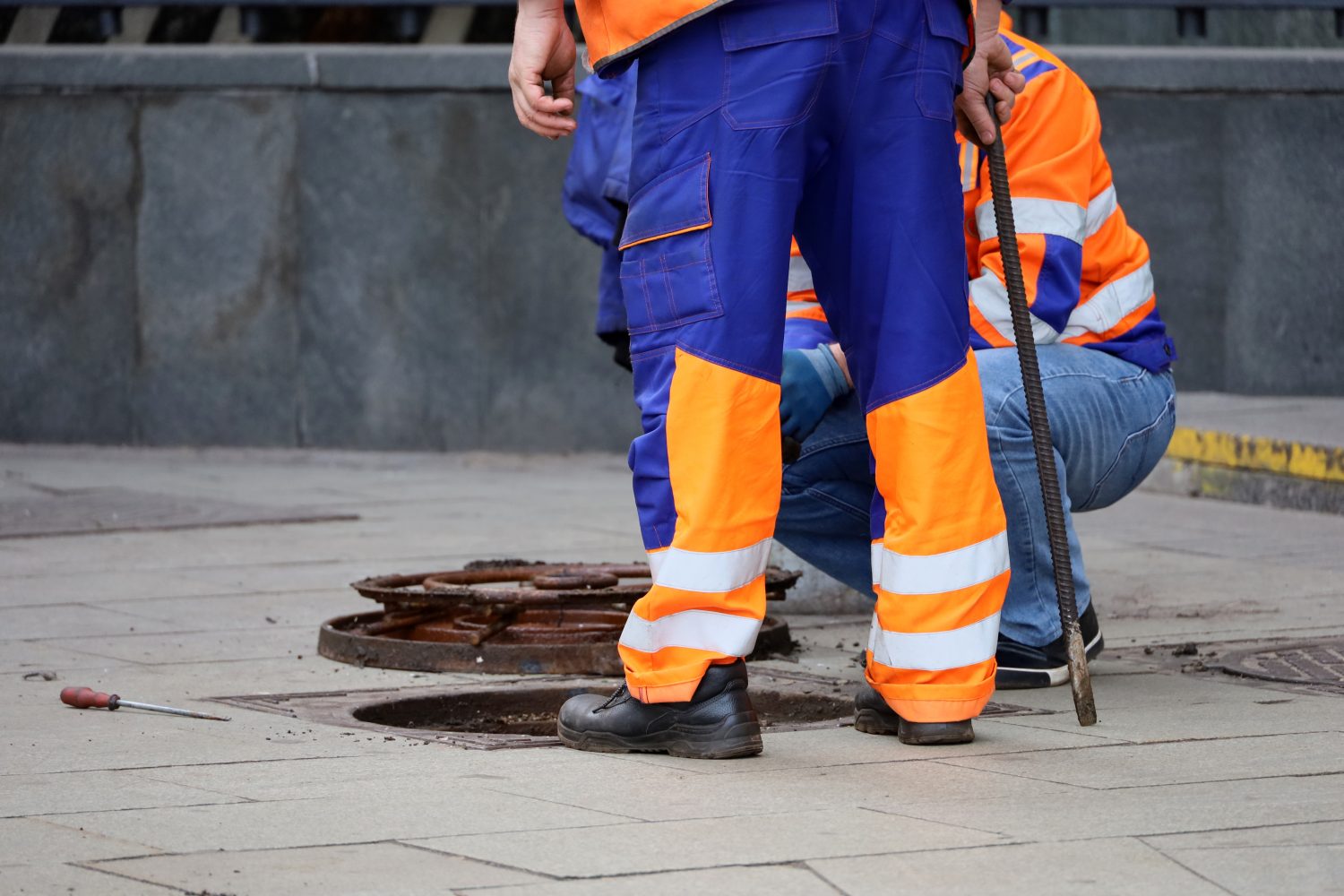 Lavoratori sopra il portello fognario aperto su una strada.  Concetto di riparazione di fognature, servizi sotterranei, sistema di approvvigionamento idrico, posa di cavi, incidente di tubature dell'acqua