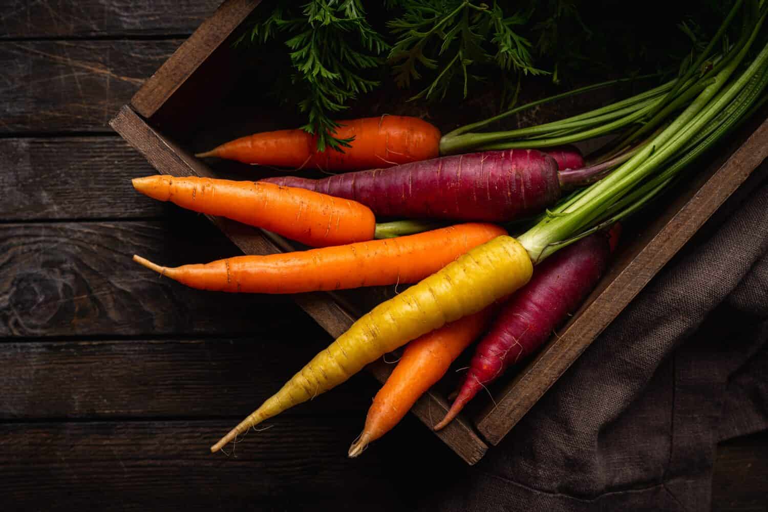 Carota arcobaleno colorata con le foglie verdi in una scatola su sfondo di legno, vista dall'alto