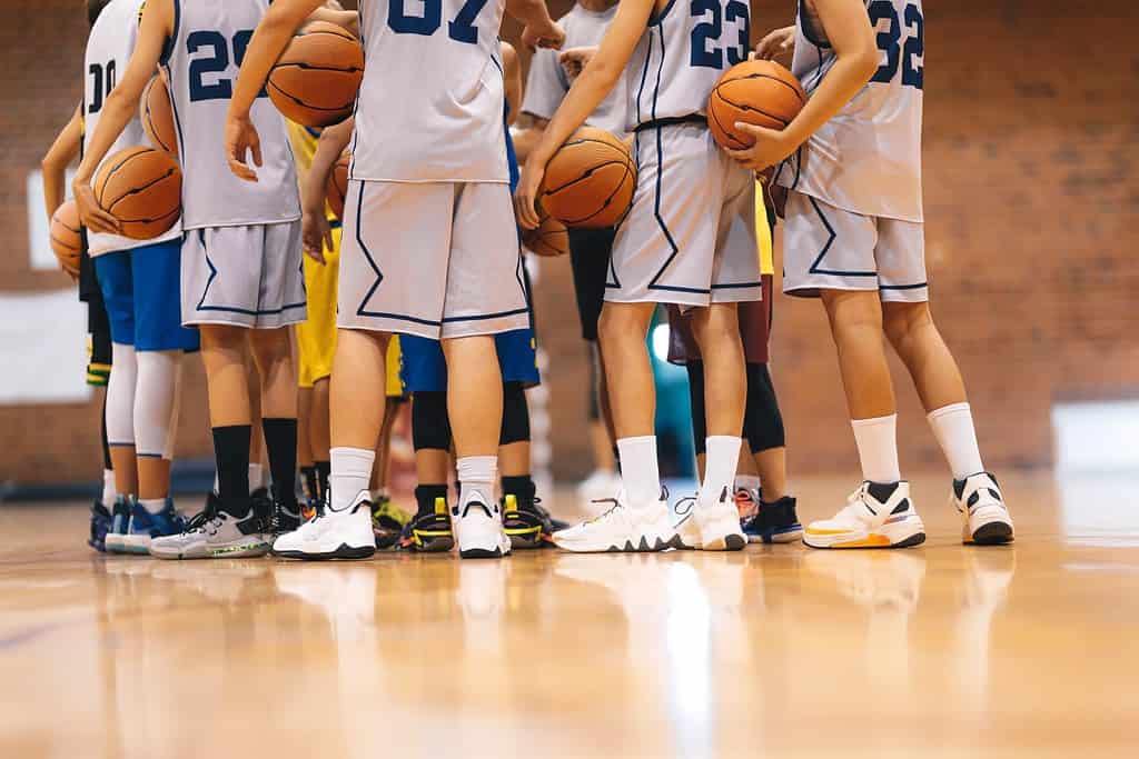 Squadra di basket junior durante la lezione di allenamento in piedi insieme e rannicchiati in cerchio.  Giocatori che ascoltano il discorso motivazionale degli allenatori prima della partita.  Squadra di basket universitaria maschile al torneo