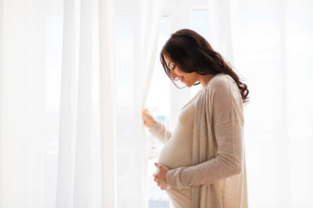 concetto di gravidanza, maternità, persone e aspettativa - primo piano di una donna incinta felice con una grande pancia alla finestra